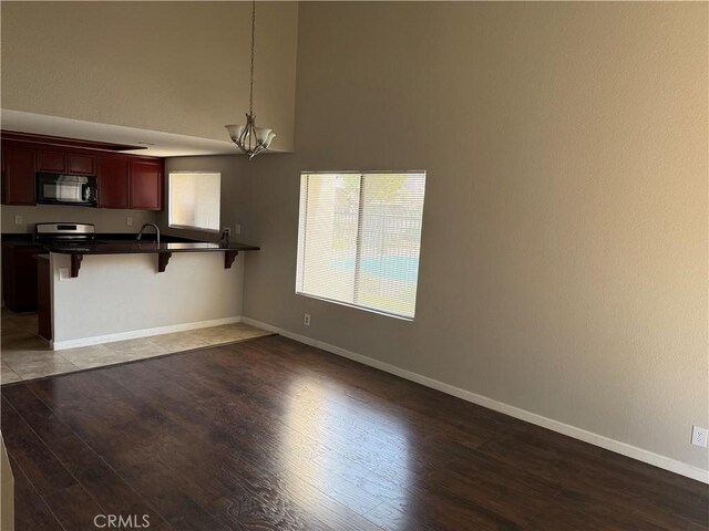 unfurnished living room featuring wood finished floors, a chandelier, baseboards, and a high ceiling