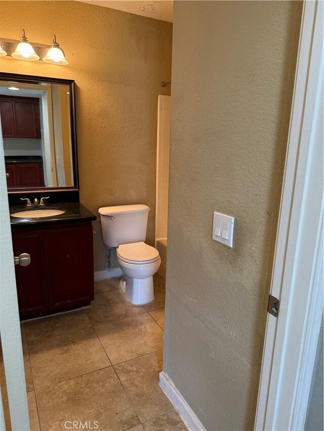 bathroom featuring a textured wall, vanity, toilet, tile patterned flooring, and washtub / shower combination