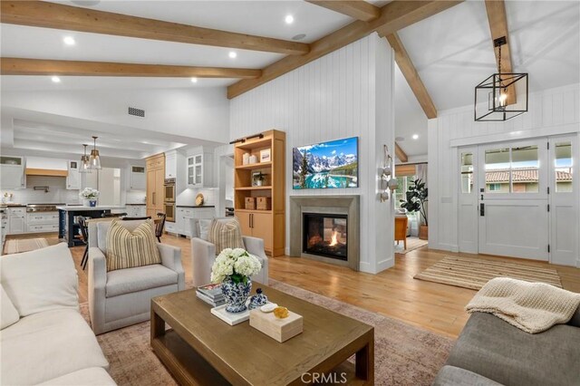 living room with a multi sided fireplace, light wood-style floors, recessed lighting, a chandelier, and beam ceiling