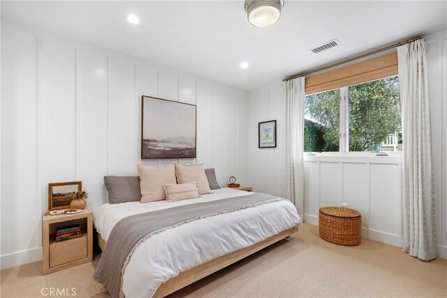 bedroom featuring light carpet, a decorative wall, and recessed lighting