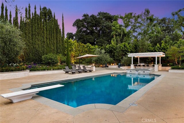 pool at dusk with a diving board, a patio, an outdoor pool, and an in-ground hot tub