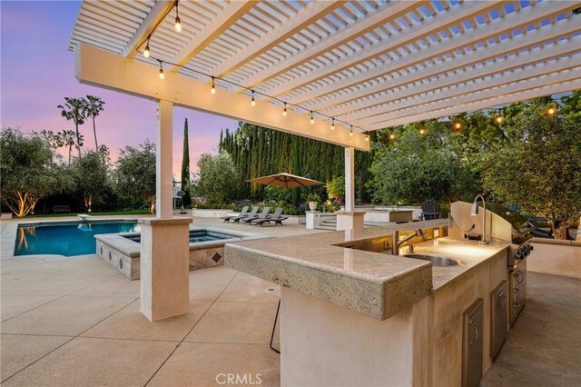 patio terrace at dusk with exterior kitchen, an outdoor pool, a sink, and an in-ground hot tub