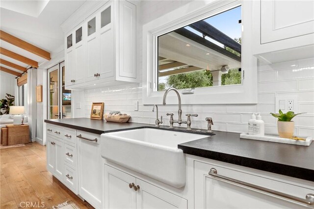 kitchen featuring a sink, dark countertops, beam ceiling, backsplash, and light wood-style floors