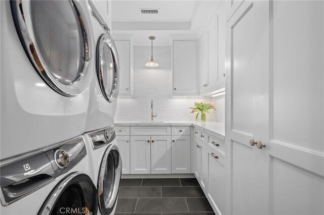 clothes washing area featuring cabinet space, dark tile patterned floors, and estacked washer and dryer