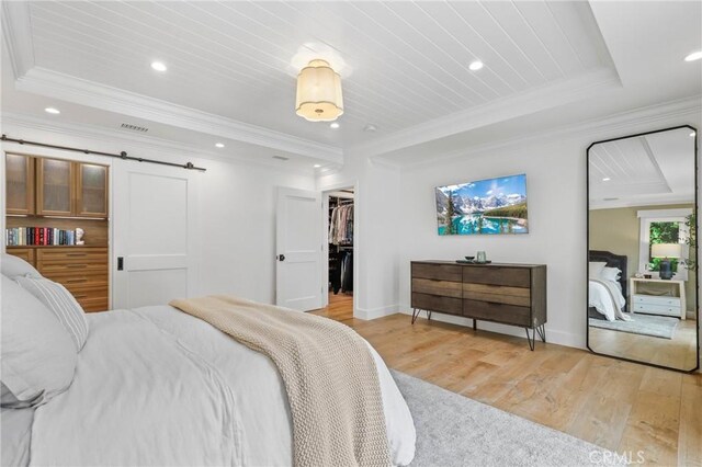 bedroom featuring light wood finished floors, a tray ceiling, baseboards, recessed lighting, and a spacious closet