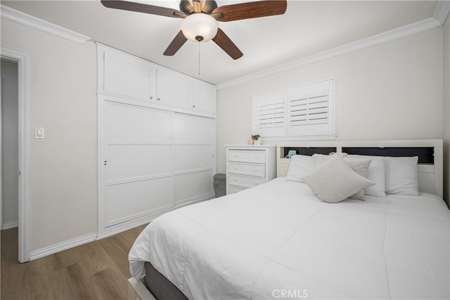 bedroom with wood finished floors, crown molding, baseboards, ceiling fan, and a closet