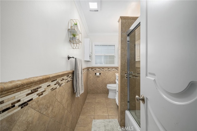 bathroom featuring tile walls, ornamental molding, toilet, combined bath / shower with glass door, and tile patterned flooring