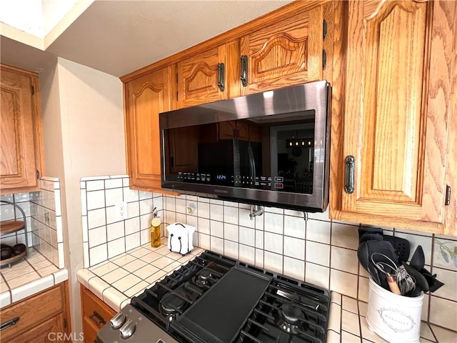 3747 Vista Campana S Unit 7, Oceanside, CA 92057 - kitchen featuring stainless steel microwave, tile countertops, gas range oven, and decorative backsplash