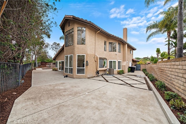24572 Wembley Cir, Laguna Hills, CA 92653 - rear view of property featuring a chimney, stucco siding, central AC unit, a patio, and a fenced backyard