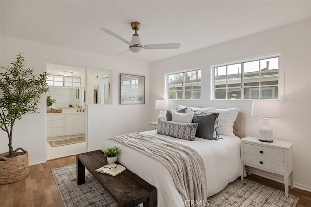 bedroom featuring light wood-style floors, ensuite bathroom, ceiling fan, and baseboards