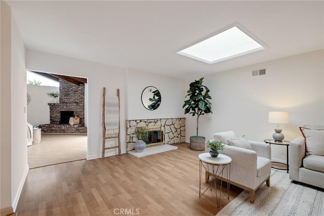 living area featuring a fireplace, light wood finished floors, a skylight, and baseboards