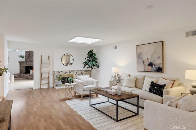 living room featuring a fireplace with raised hearth, a skylight, light wood-type flooring, and baseboards
