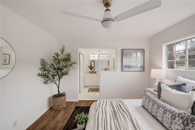 bedroom featuring wood finished floors, ensuite bath, baseboards, and a ceiling fan