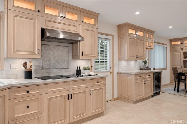 kitchen featuring under cabinet range hood, beverage cooler, black electric stovetop, tasteful backsplash, and light stone countertops
