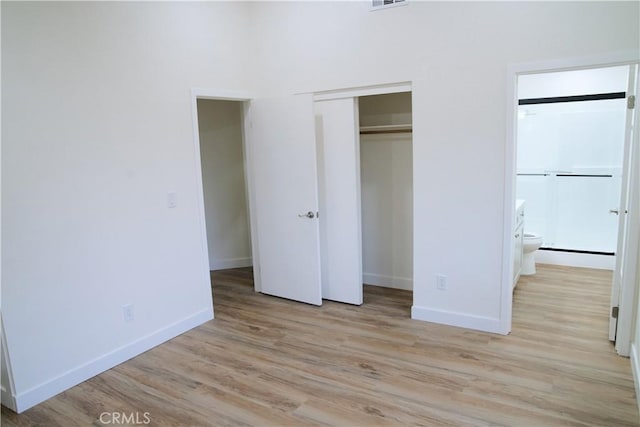 unfurnished bedroom with light wood finished floors, a closet, baseboards, and connected bathroom