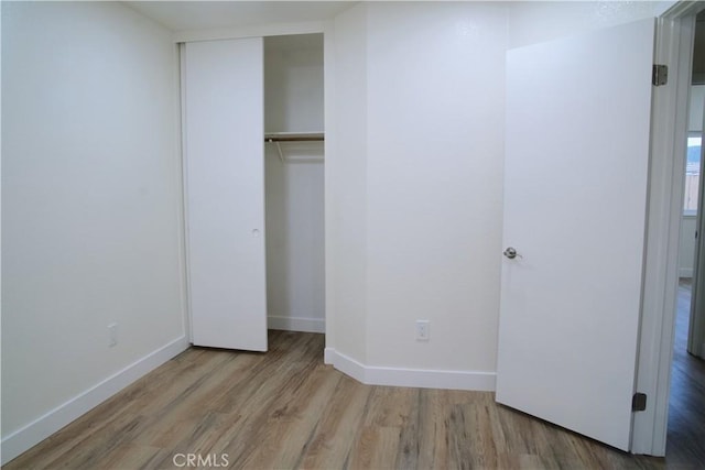 unfurnished bedroom featuring wood finished floors, baseboards, and a closet