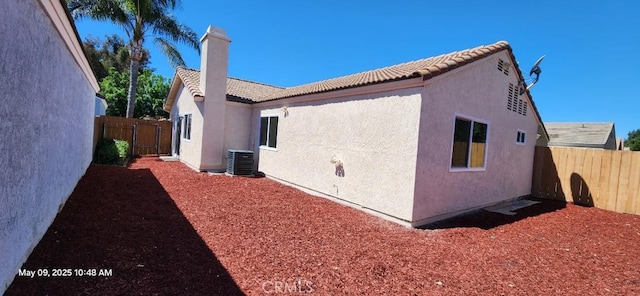 view of side of property featuring central air condition unit, a fenced backyard, stucco siding, and a tile roof