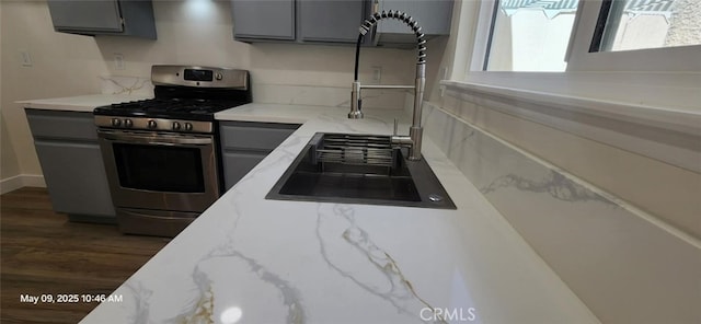 kitchen featuring stainless steel gas range, gray cabinetry, dark wood-type flooring, and light stone countertops