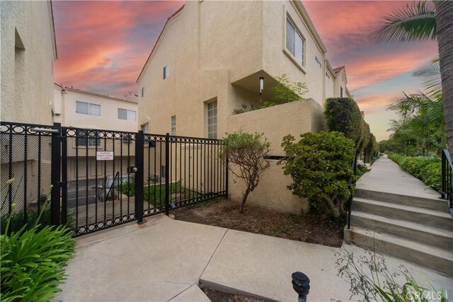 property exterior at dusk featuring stucco siding, fence, and a gate