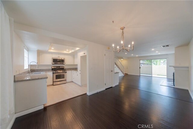 kitchen featuring stainless steel appliances, open floor plan, a chandelier, light wood-style flooring, and white cabinets