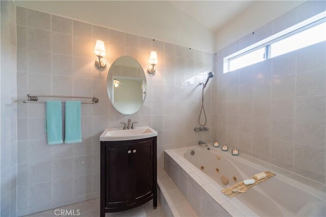bathroom with vanity, a combined bath / shower with jetted tub, and tile walls