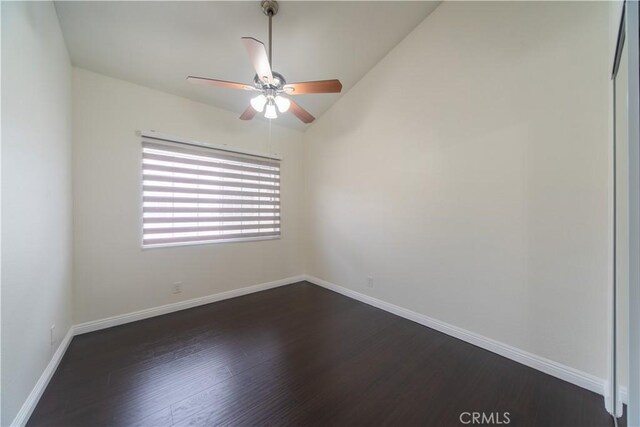 spare room with a ceiling fan, dark wood-style floors, baseboards, and vaulted ceiling
