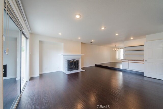 unfurnished living room featuring a chandelier, dark wood-style floors, a fireplace with flush hearth, and recessed lighting