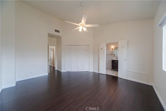 unfurnished bedroom with dark wood finished floors, baseboards, a closet, a towering ceiling, and ceiling fan