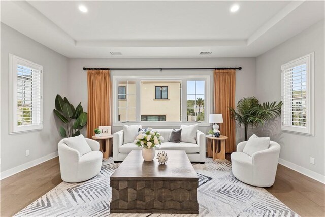 living area featuring a tray ceiling, wood finished floors, baseboards, and recessed lighting
