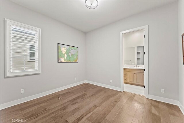 unfurnished bedroom featuring light wood finished floors, a sink, baseboards, and ensuite bathroom