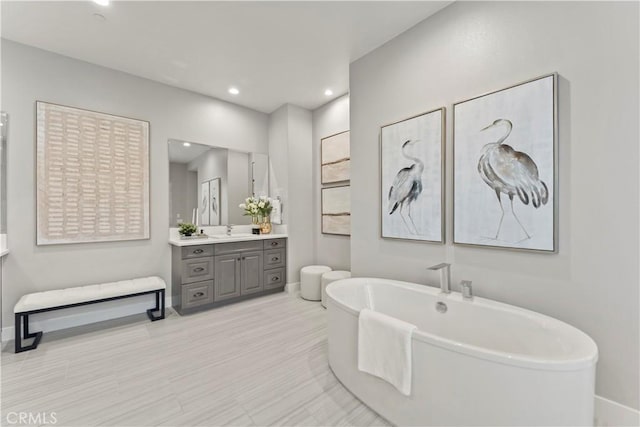full bath with baseboards, vanity, a soaking tub, and recessed lighting