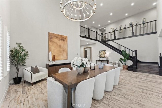 dining space featuring a towering ceiling, wood finished floors, stairway, a chandelier, and recessed lighting