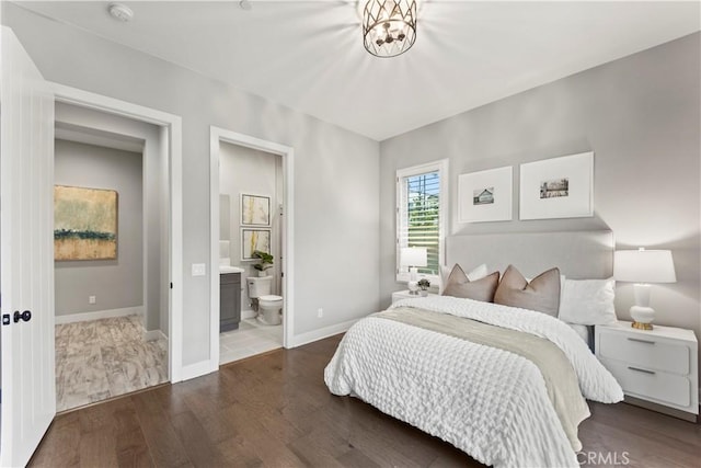 bedroom with wood finished floors, baseboards, ensuite bath, and a chandelier