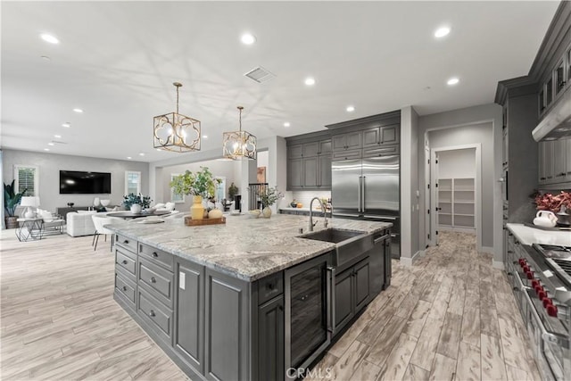 kitchen with beverage cooler, recessed lighting, light wood-type flooring, a sink, and a large island with sink