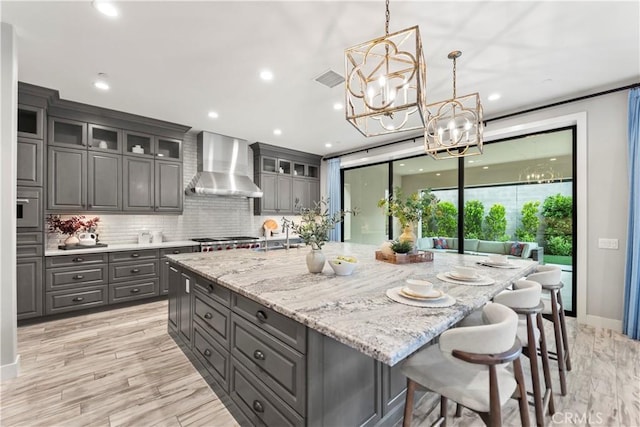 kitchen with wall chimney exhaust hood, gray cabinets, a chandelier, a large island, and glass insert cabinets