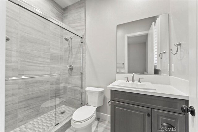 bathroom featuring toilet, a stall shower, vanity, and baseboards