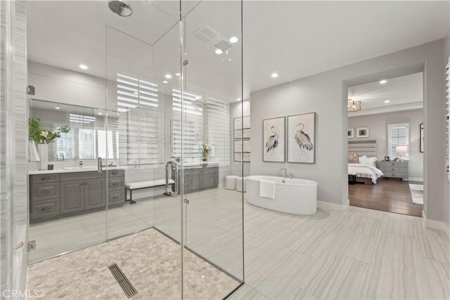 ensuite bathroom with a stall shower, a soaking tub, recessed lighting, vanity, and baseboards