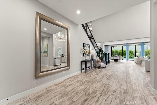 corridor with a chandelier, wood finished floors, recessed lighting, baseboards, and a towering ceiling