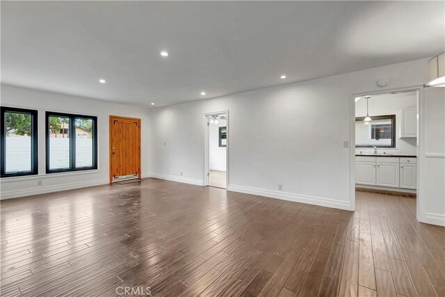 unfurnished living room with dark wood-type flooring, recessed lighting, baseboards, and a sink