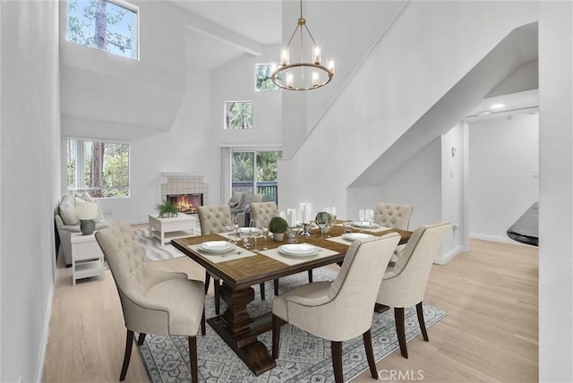 dining room with light wood finished floors, a towering ceiling, a chandelier, a tiled fireplace, and baseboards