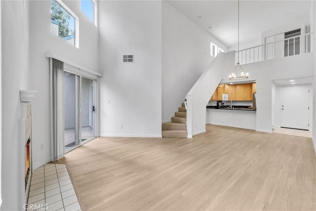 unfurnished living room featuring a high ceiling, a chandelier, stairs, baseboards, and light wood finished floors