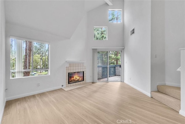 unfurnished living room featuring high vaulted ceiling, stairway, light wood-type flooring, a tiled fireplace, and baseboards