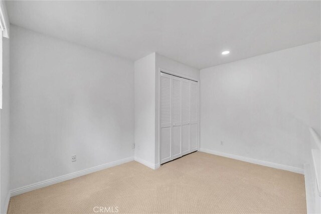 unfurnished bedroom with light carpet, a closet, recessed lighting, and baseboards
