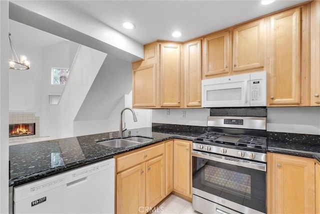 kitchen featuring white appliances, a sink, light brown cabinets, dark stone counters, and recessed lighting