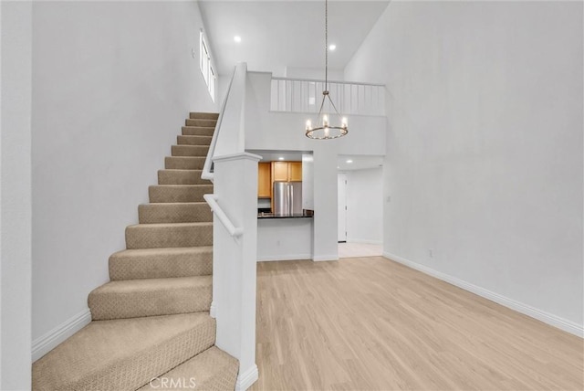 stairway with a chandelier, a towering ceiling, wood finished floors, and baseboards