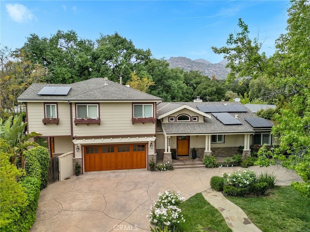 view of front of home with roof mounted solar panels, driveway, a garage, stone siding, and roof with shingles