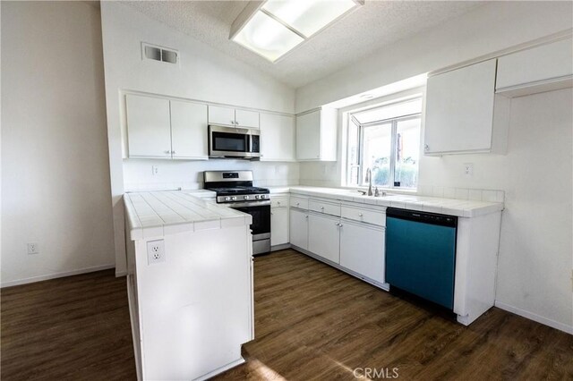 kitchen with stainless steel appliances, tile counters, lofted ceiling, dark wood-style floors, and white cabinets