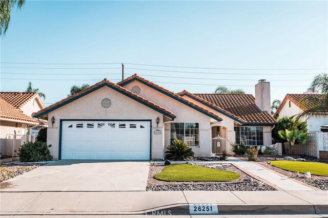 view of front of house featuring stucco siding, a garage, concrete driveway, a tile roof, and a chimney