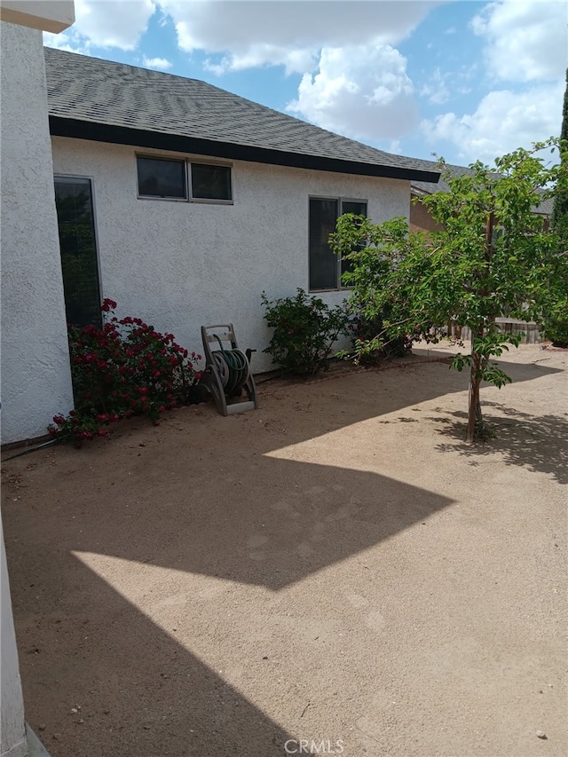 17795 Stevens Rd, Adelanto, CA 92301 - view of side of property featuring stucco siding, a shingled roof, and a patio area