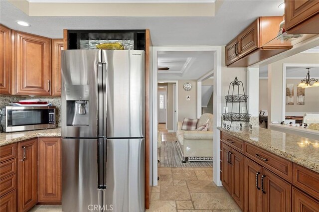 13545 Anchor Dr, Victorville, CA 92395 - kitchen featuring appliances with stainless steel finishes, a raised ceiling, brown cabinetry, stone tile floors, and light stone countertops